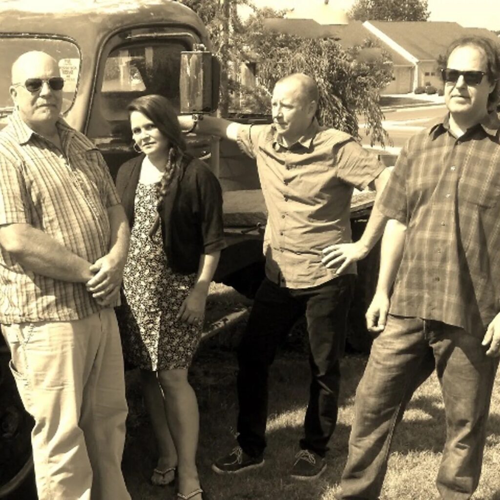 Group photo of The Rogue Farmers band members standing in front of an old truck in a vintage, sepia-toned setting.