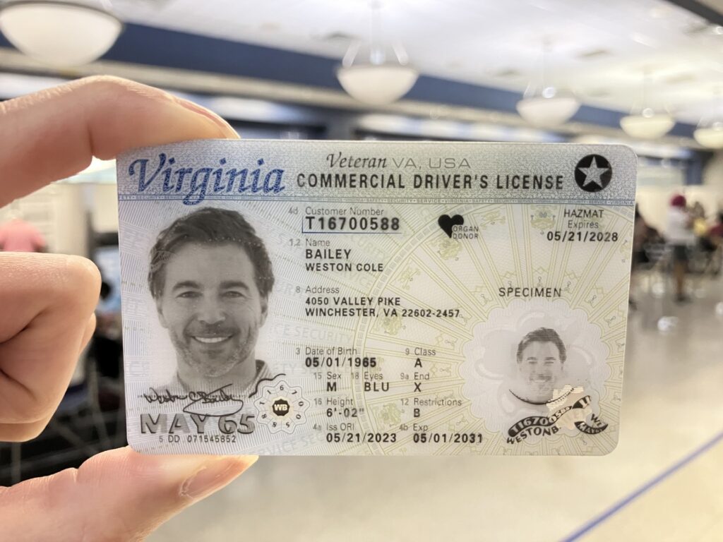 Hand holding a sample Virginia commercial driver’s license featuring the REAL ID star marking in the top right corner.